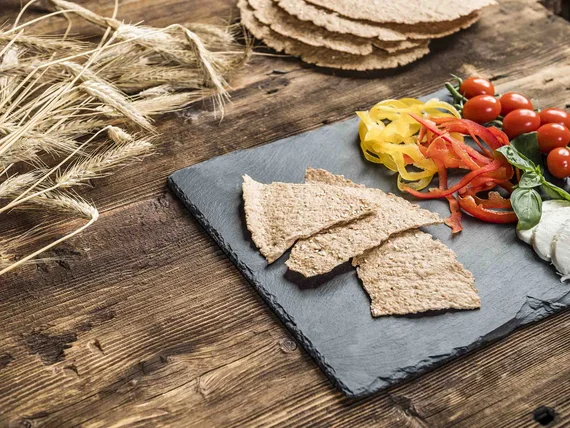 Cracker integrali croccanti con peperoni, pomodori ciliegia e mozzarella su lastra di ardesia