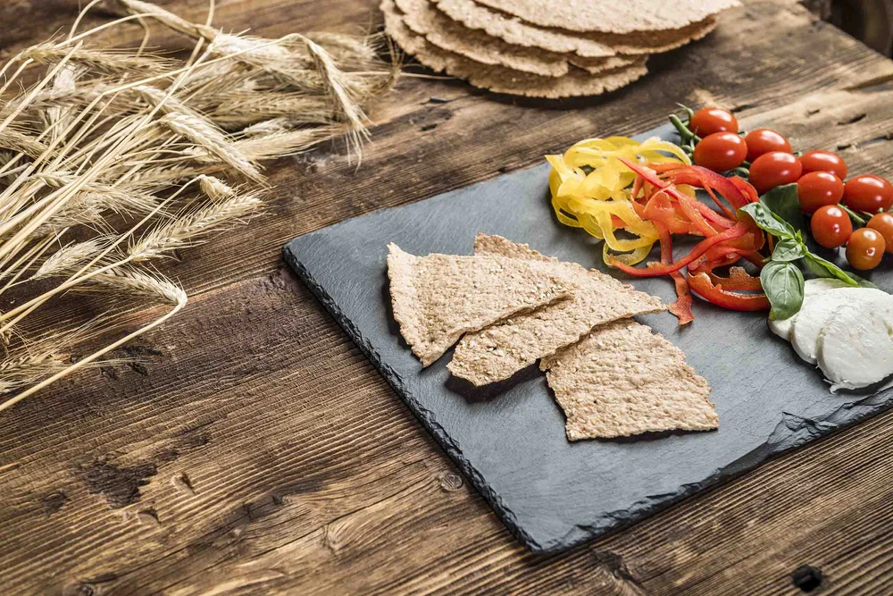 Cracker integrali croccanti con peperoni, pomodori ciliegia e mozzarella su lastra di ardesia